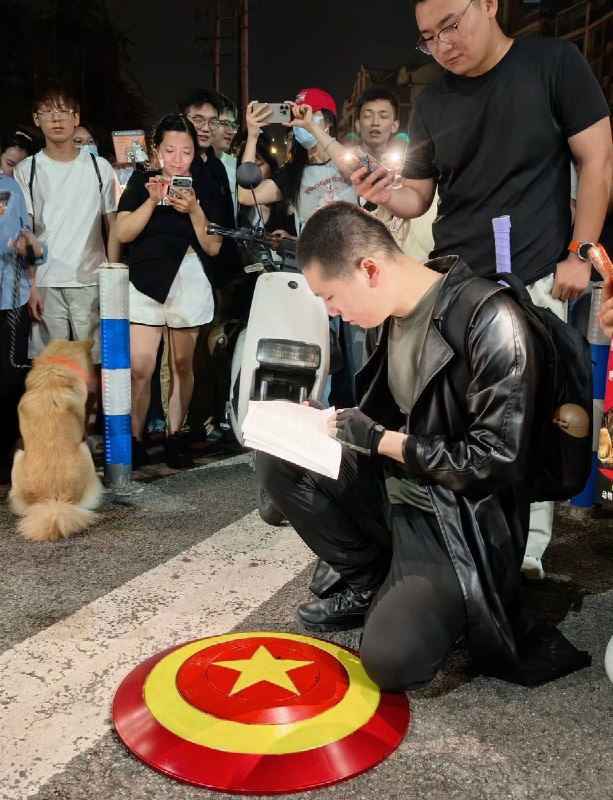 6月9日晚，重庆“山姆打包哥”虐狗事件现场，有人阅读刑法一本通，群众给他打灯翻阅